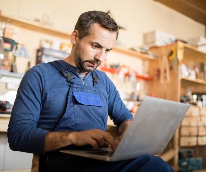 Small business owner in a workshop signing paperwork on a laptop